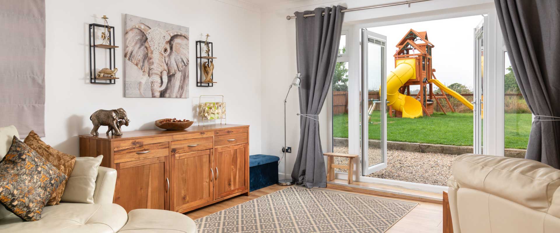Bright living room with open doors leading to a private garden and playground.