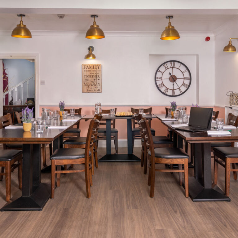 A spacious grand dining hall with long wooden tables and brass lighting at the Big Pink House.
