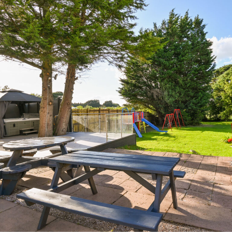 Outdoor paved patio with picnic benches and a view of the playground at the Big Pink House.