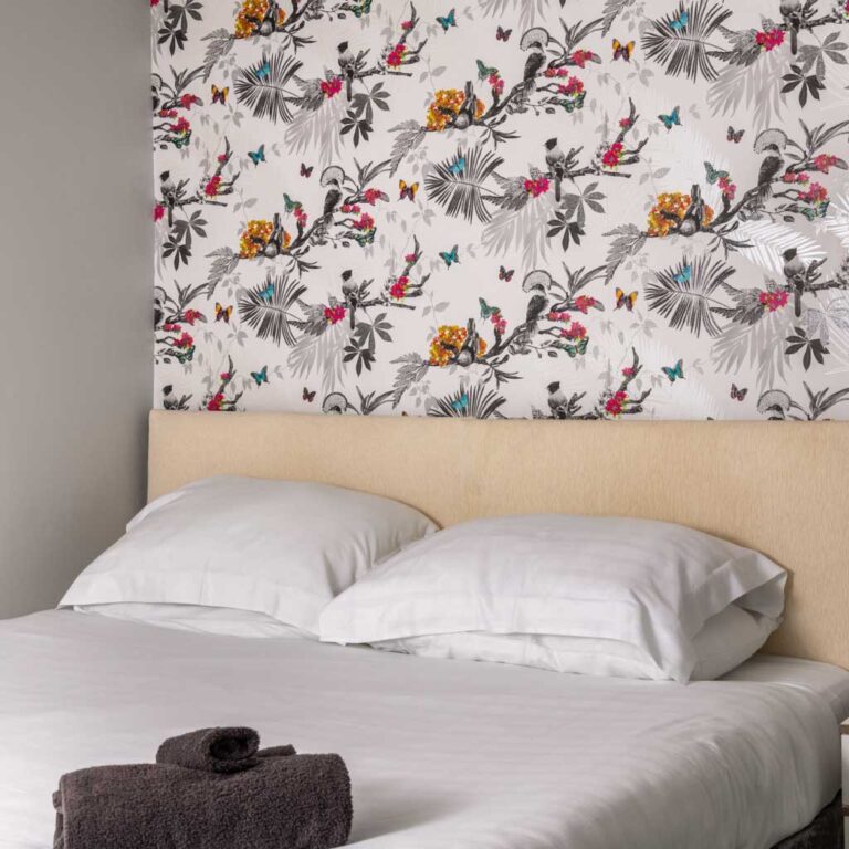 Modern bedroom with white bedding and a bold bird-and-flower botanical feature wall.