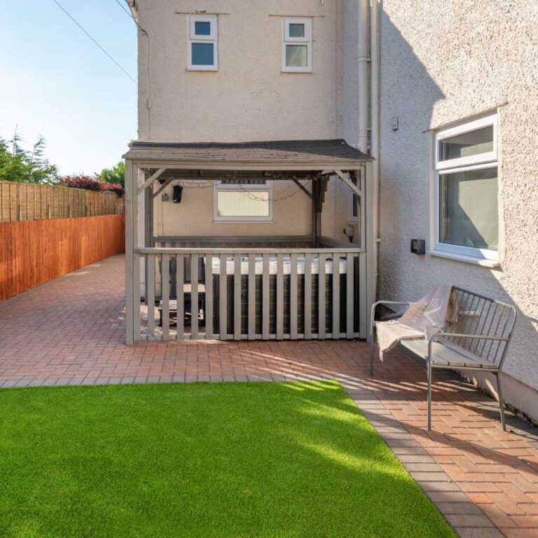 An enclosed private garden featuring artificial grass, a brick patio, and a sheltered hot tub.