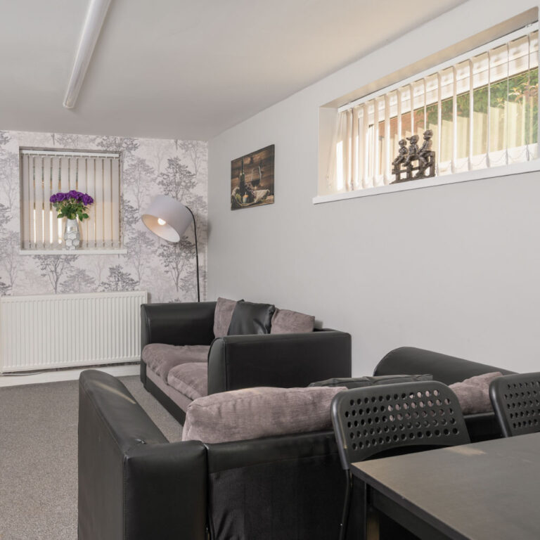 Modern lounge area with grey and black sofas, a large floor lamp, and a wall-mounted fireplace.