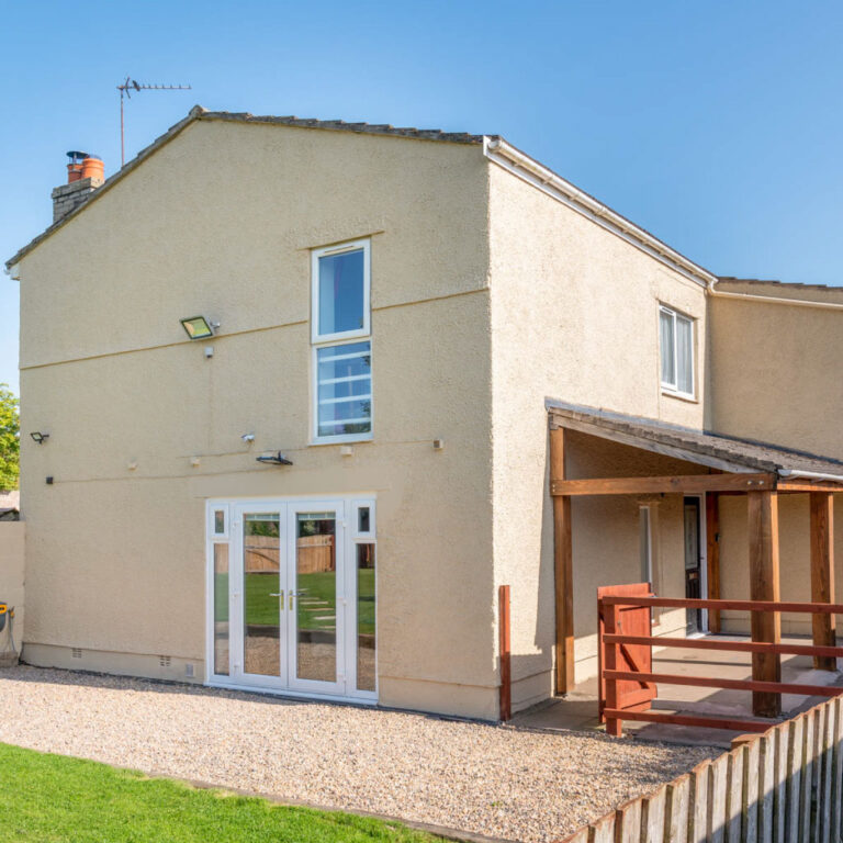 Exterior view of a cream-coloured cottage with white French doors and a timber porch.