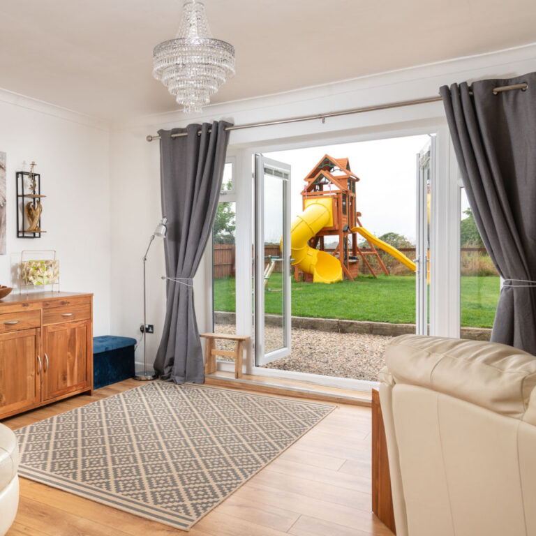 A bright cottage lounge with open doors leading to a private garden and playground.