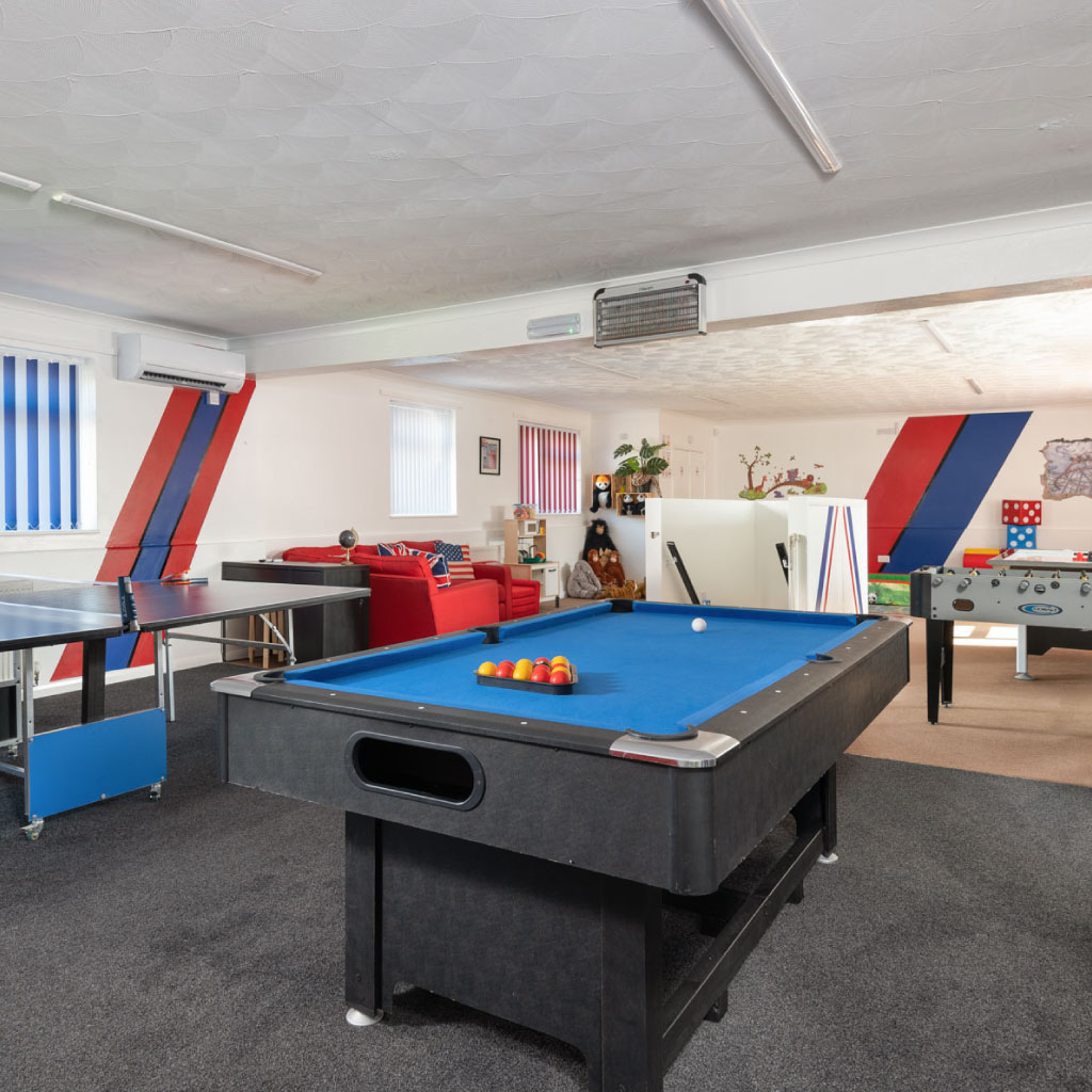 A large indoor games room featuring a pool table, ping pong table, and foosball.