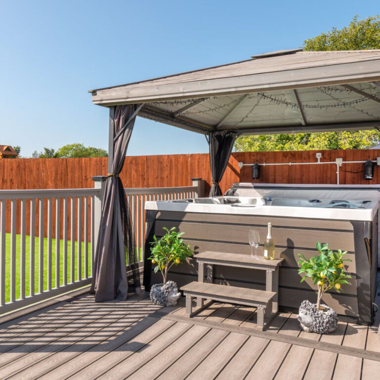 A hot tub under a gazebo on a grey deck with a bottle of champagne ready.