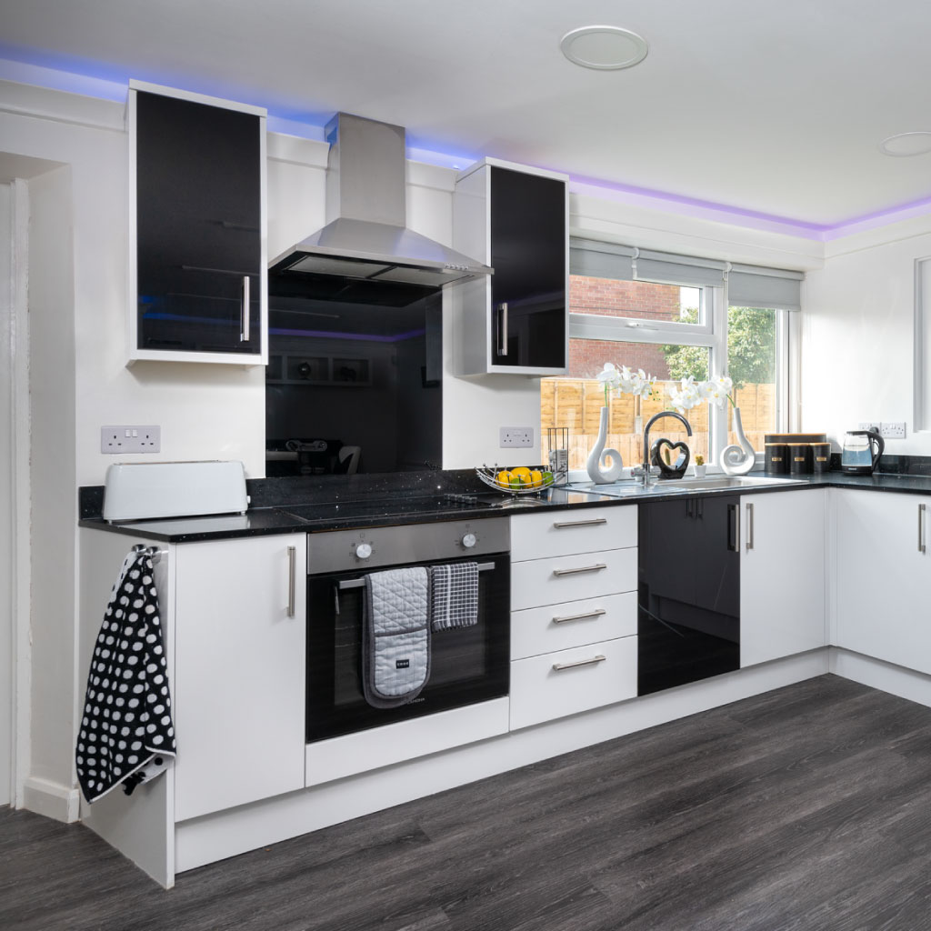 Modern white and black kitchen with blue LED accent lighting and dark wood-effect flooring.